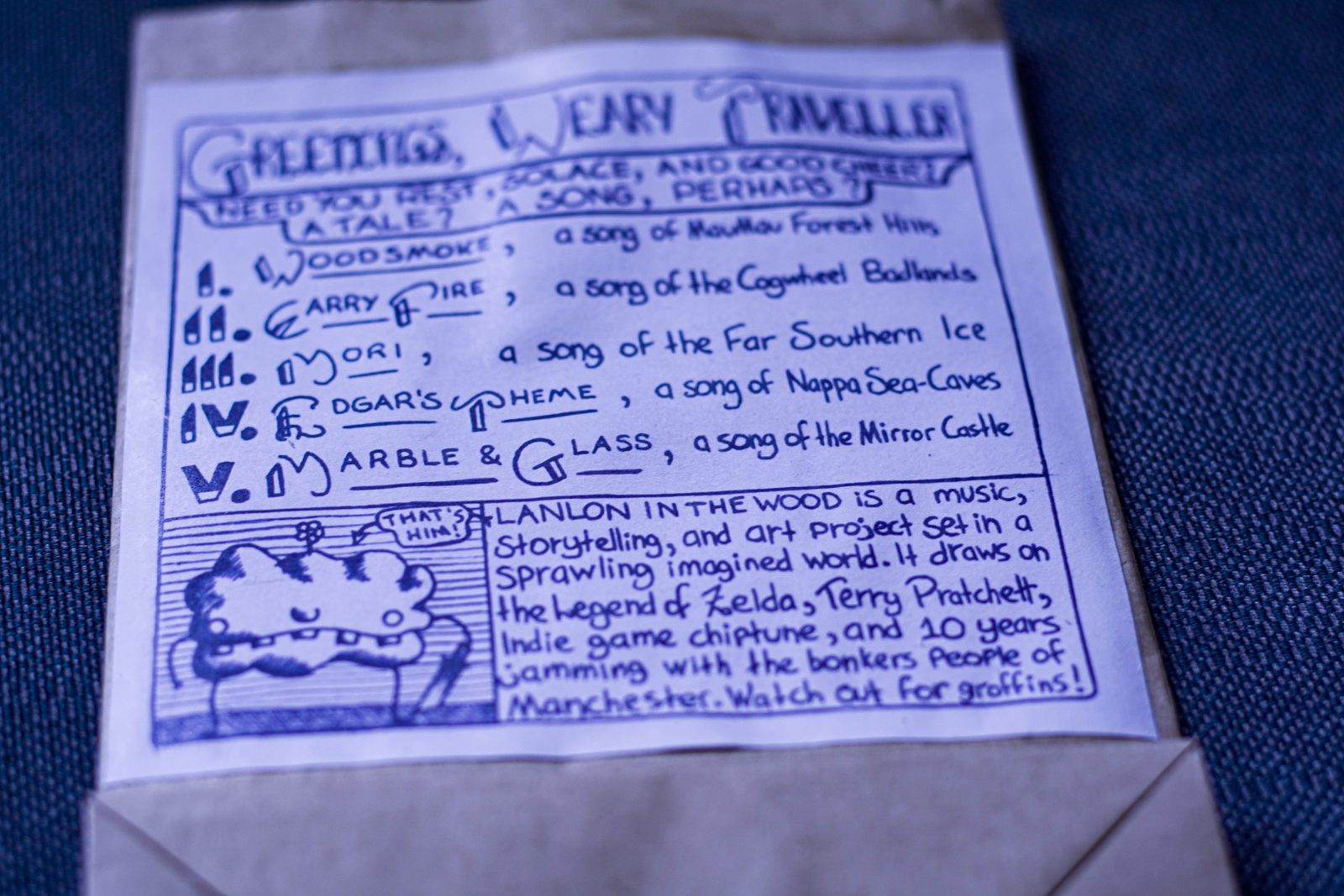 Handwritten letter beginning 'Greetings weary traveller', listing the album's songs and the places they come from, on a paper envelope.