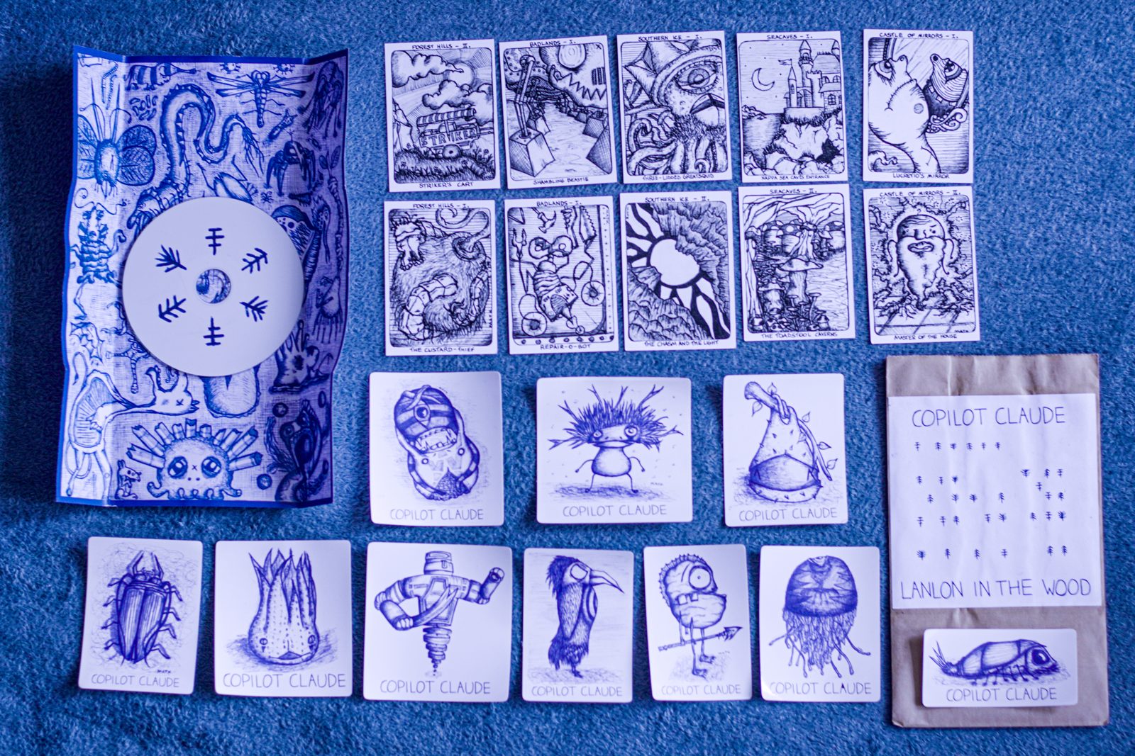 The full physical edition laid out on a blue cloth: hand-made cover, ten story cards, stamped cards and the CD sleeve.